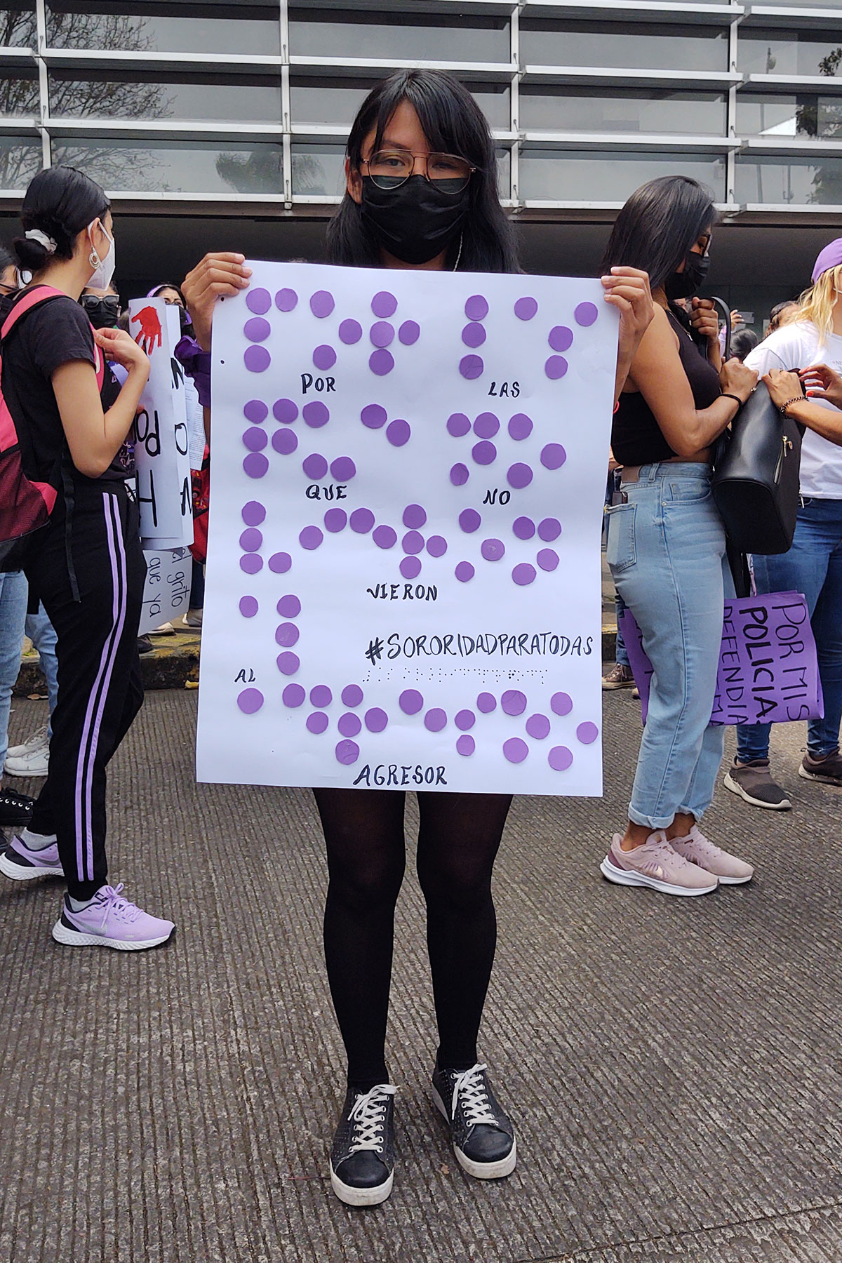 Fotografía. Pancarta en Braille en la marcha del #8M de 2022 en Veracruz. Descripción: Una mujer en la marcha del 8M sostiene una cartulina que dice “Por las que no vieron al agresor” en Braille. Crédito: Aislinn Bello